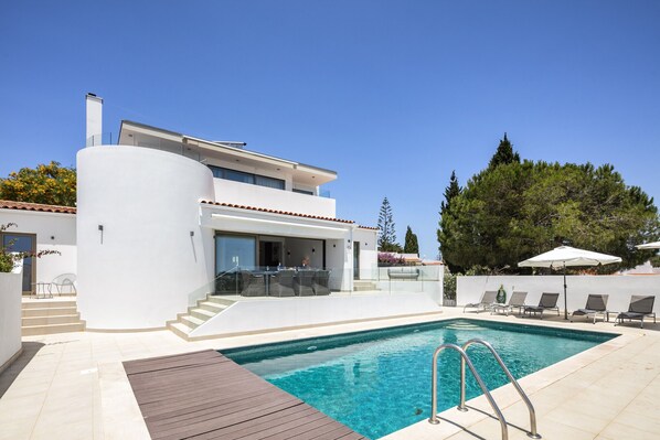 Una casa moderna con piscina, zona de estar exterior y una escalera que lleva al piso superior.