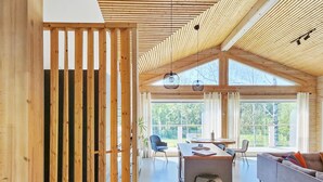 Une pièce spacieuse avec un plafond haut, des poutres en bois, un coin repas avec une table et des chaises, et un canapé agrémenté de coussins colorés.