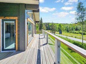 A wooden deck with glass doors and windows, overlooking a green landscape and a road.