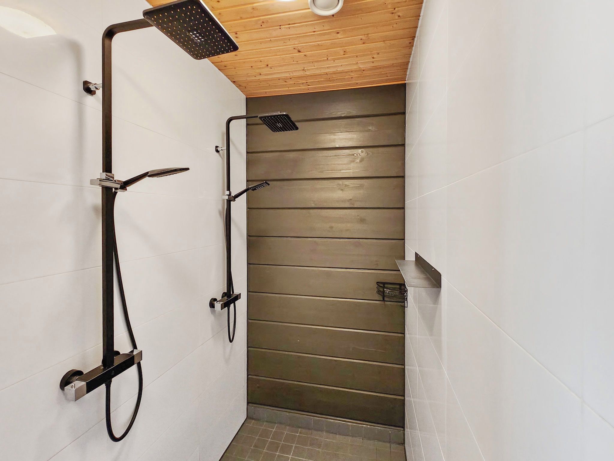 A narrow shower area with a wooden ceiling, white tiled walls, and a tiled floor.