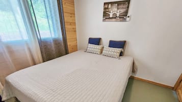 Ein Zimmer mit einem großen Bett, zwei Kissen, einem Wandbild und einem Fenster mit Vorhängen.
