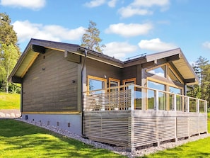 Une maison moderne dotée d’une grande terrasse, de nombreuses fenêtres et d’un toit en pente.