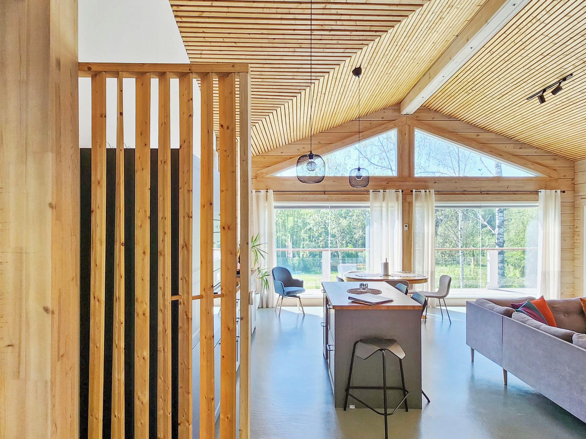 A modern interior with a wooden ceiling, large windows, a dining area, and a seating area.