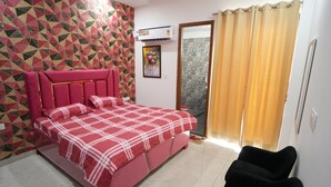 A bedroom with a bed, a black chair, a patterned wall, and a window with curtains. - Aerostays Mohali (Dera Bassi)
