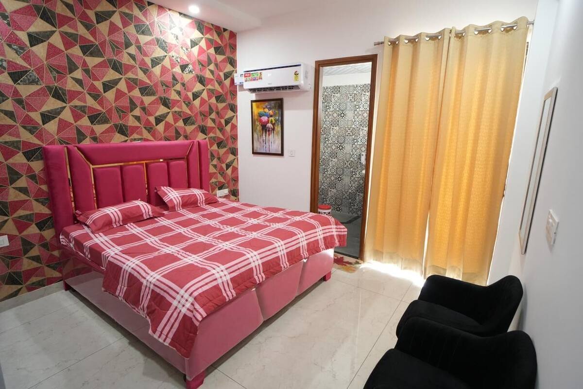 A bedroom with a bed, a black chair, a patterned wall, and a window with curtains.