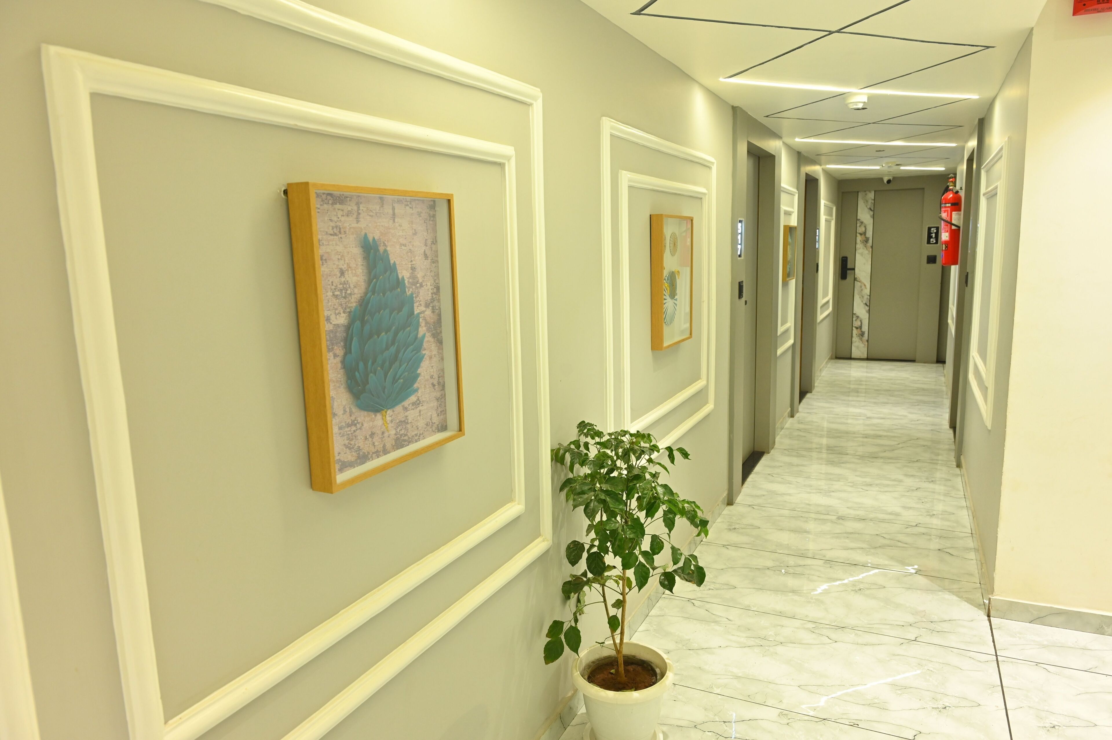 A hallway with framed artwork on the walls, a potted plant, and a marble floor.