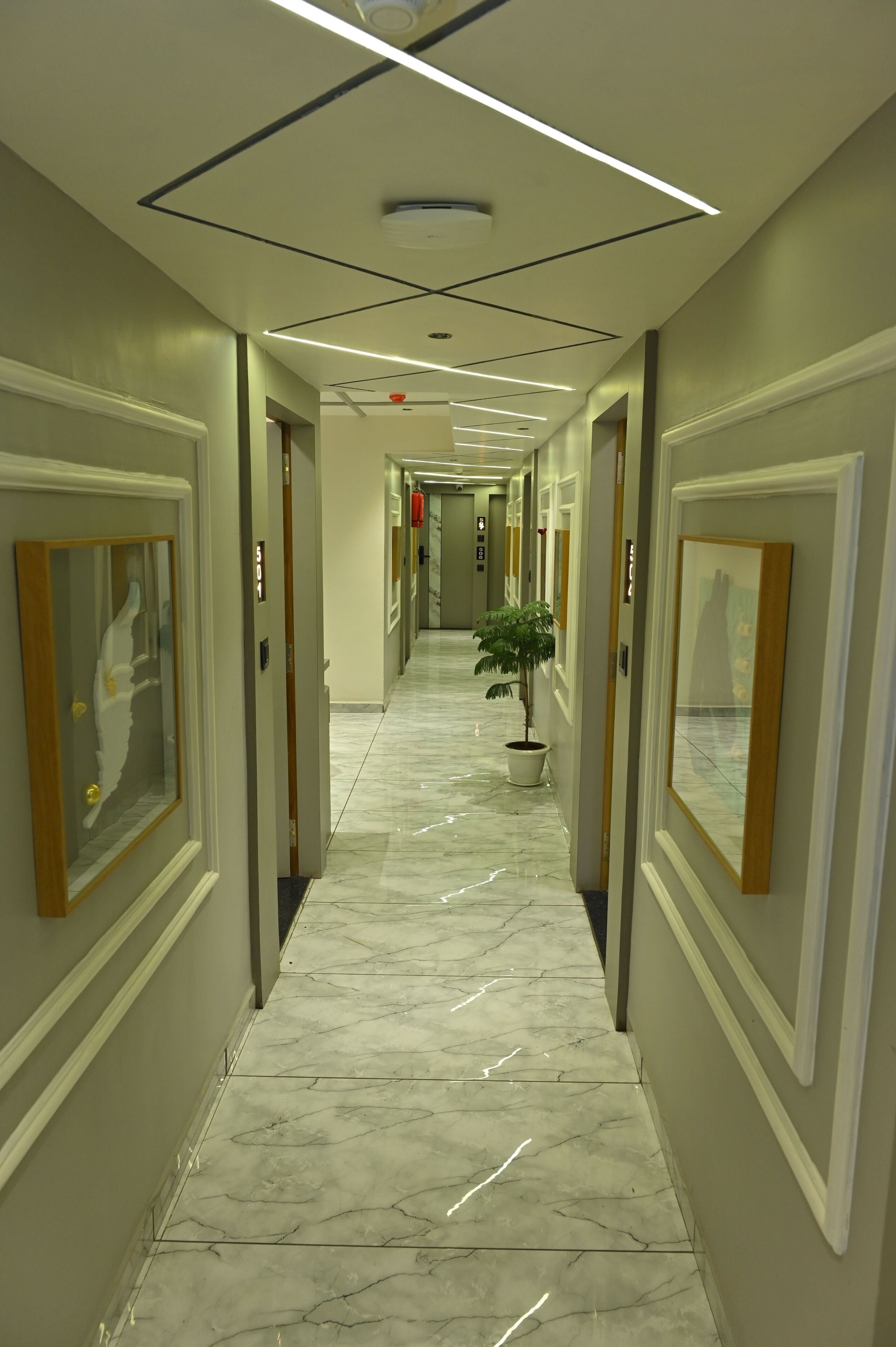 Un pasillo de hotel con suelo de mármol, obras de arte enmarcadas y una planta en maceta.