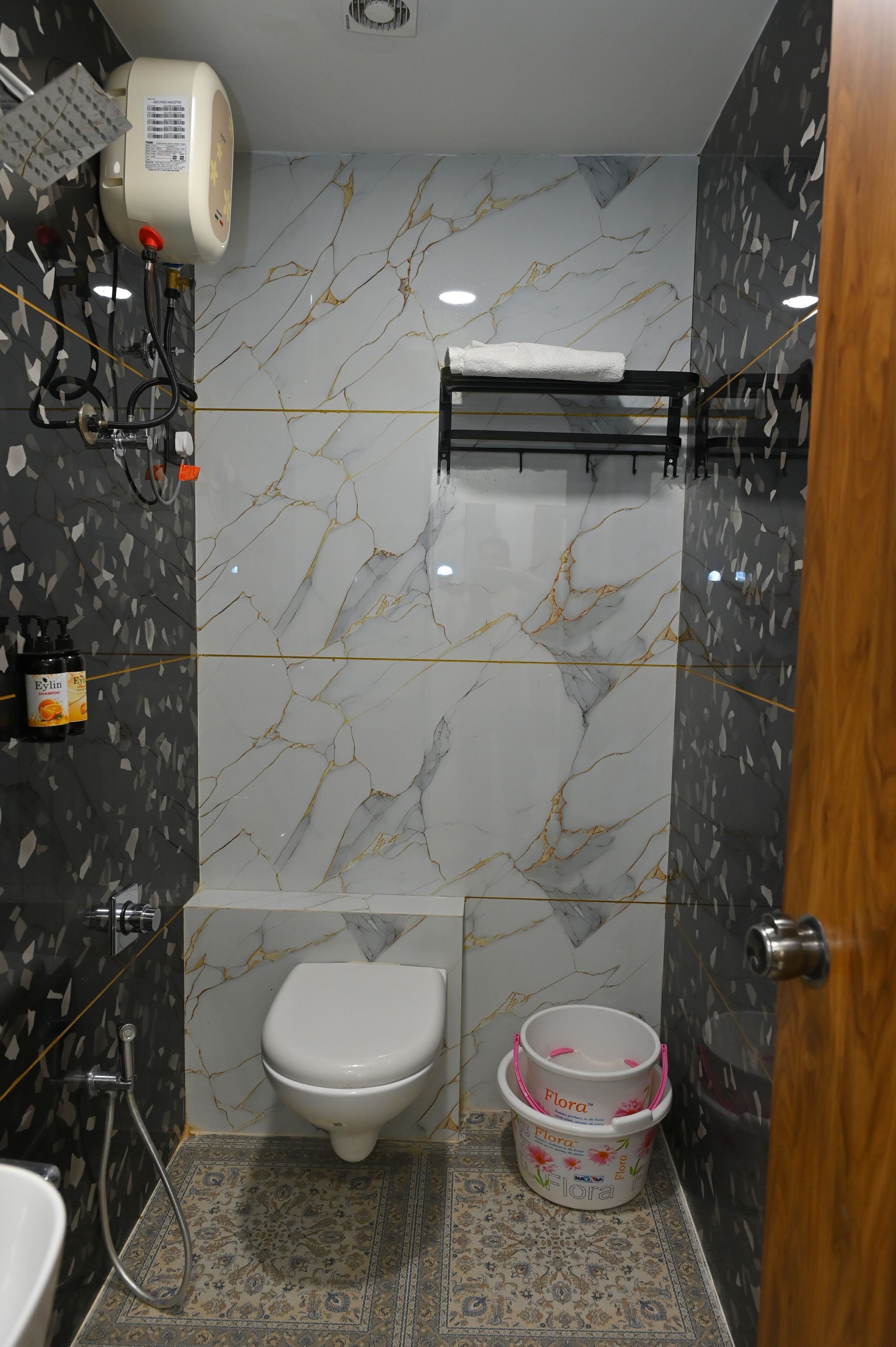 Casa de banho com sanita, secador de mãos, chuveiro e um balde decorativo.