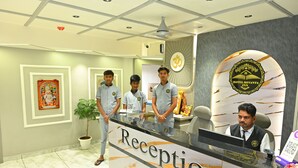 A hotel reception desk with a 'Reception' sign, a receptionist, and three staff members in uniform. - Hotel Revanta Inn (Ahmedabad)