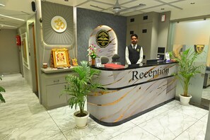 En receptionsdisk med en logotyp, en inramad bild, en vas med blommor och två krukväxter.