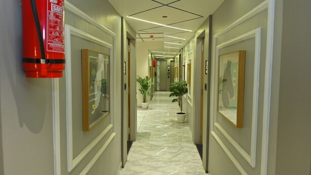 A corridor with a fire extinguisher, framed pictures, and potted plants. - Hotel Revanta Inn (Ahmedabad)