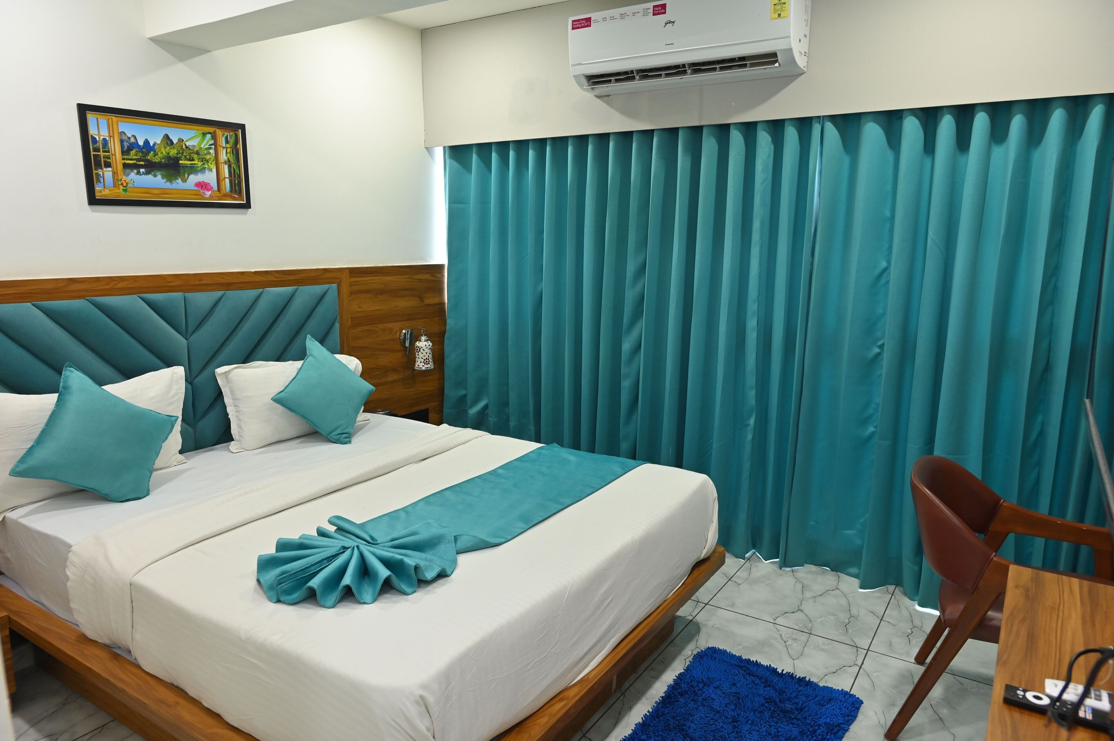 A neatly made bed with teal and white bedding, a wooden headboard, a blue rug, a wooden chair, and a painting on the wall.