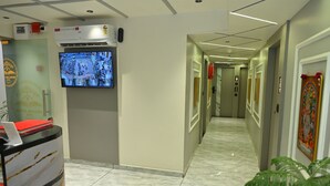 A hotel hallway with a reception desk, a mounted television, and a long corridor with doors and elevators. - Hotel Revanta Inn (Ahmedabad)