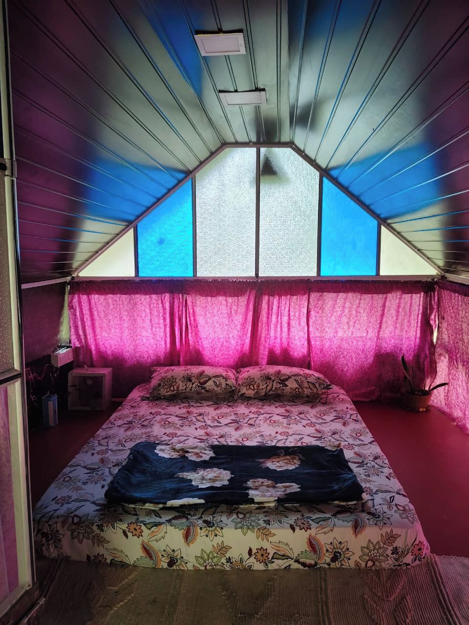 A bedroom with a sloped ceiling, a bed with floral bedding, a nightstand, and a potted plant.
