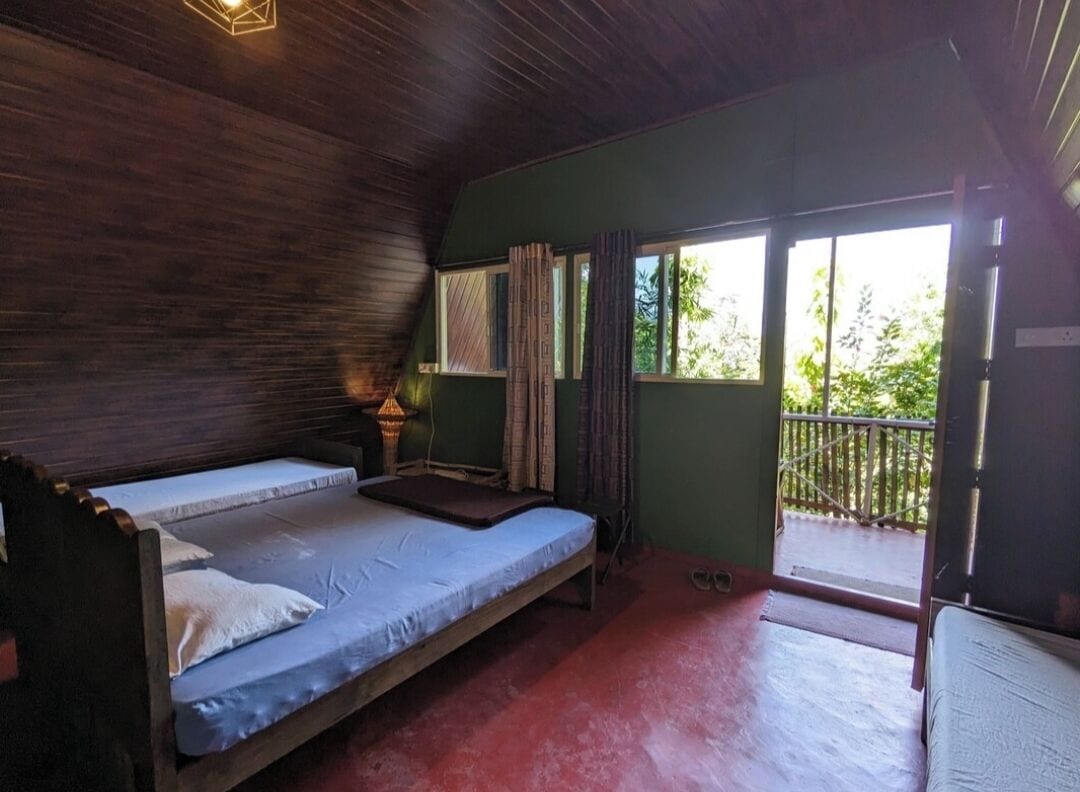 Una habitación con dos camas individuales, techo de madera, ventana con cortinas y balcón con barandilla.