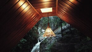 A wooden ceiling with a hanging light fixture and a view of a waterfall through a window. - Hornbill Paradise Munnar (Devikolam)