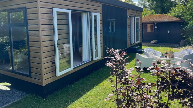Een modern houten huis met twee verdiepingen, grote schuifpuien en een klein bijgebouw.