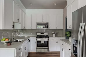 Una cocina moderna con armarios blancos, electrodomésticos de acero inoxidable, un fregadero y una encimera con un frutero.