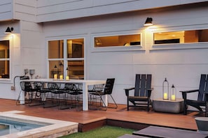 Un espacio al aire libre con piscina, mesa, sillas e iluminación ambiental.