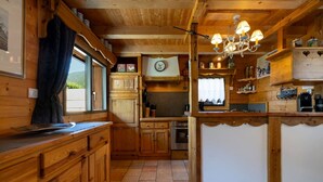 Interior de una cabaña de madera con cocina, comedor y un ventanal grande con vistas a un paisaje pintoresco.