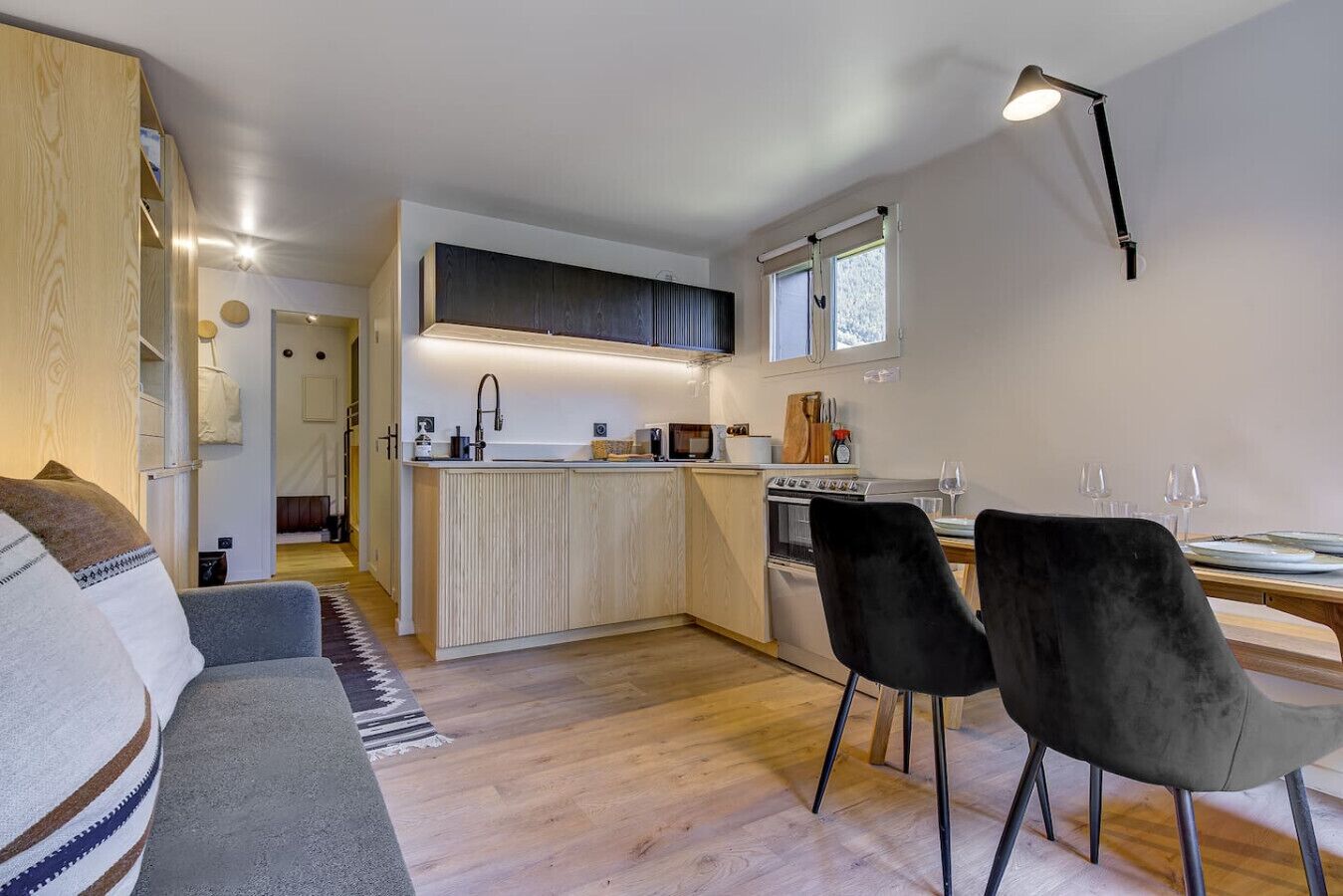 A modern kitchen with a central island, a dining area with two chairs, and a sofa in a living room.