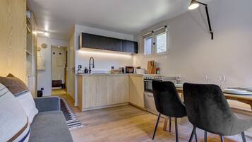 A modern kitchen with a central island, a dining area with two chairs, and a sofa in a living room.