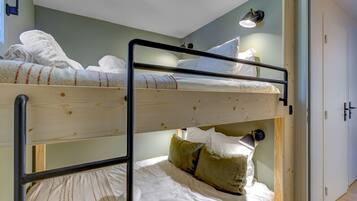 A bunk bed room with two beds, a wooden floor, a white door, and a wall-mounted light fixture.