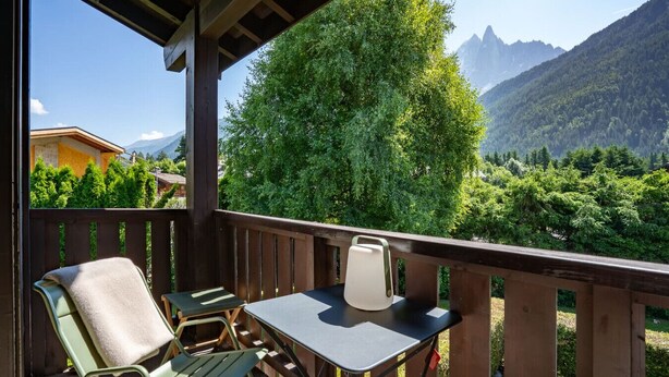 Un balcón con mesa y sillas, con vistas a un paisaje montañoso de vegetación densa.