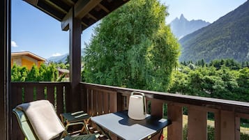 A balcony with a table and chairs, overlooking a mountainous landscape with dense greenery.