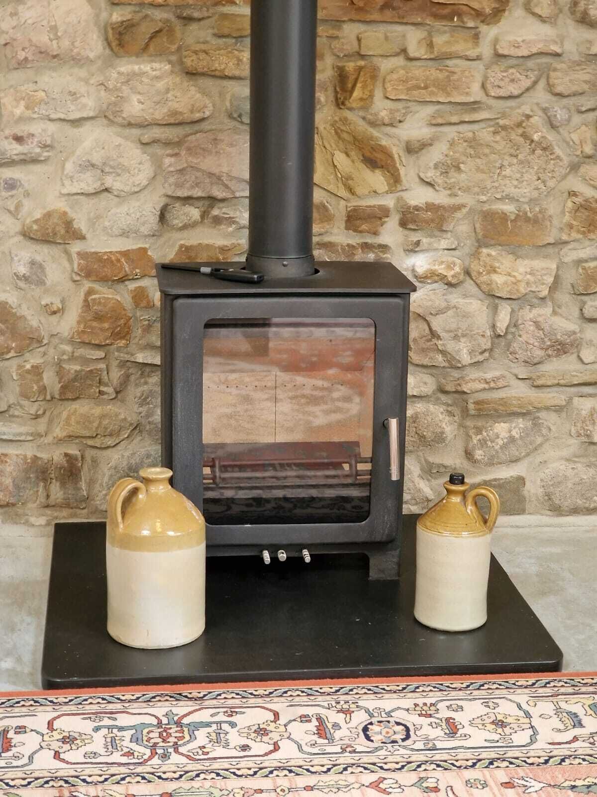 A wood-burning stove with two ceramic containers on either side, set against a stone wall background.