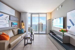 Ein modernes Wohnzimmer mit Sofa, Couchtisch und Fernseher. Es zeigt Kunstwerke, eine Pflanze und Blick auf die Stadt.