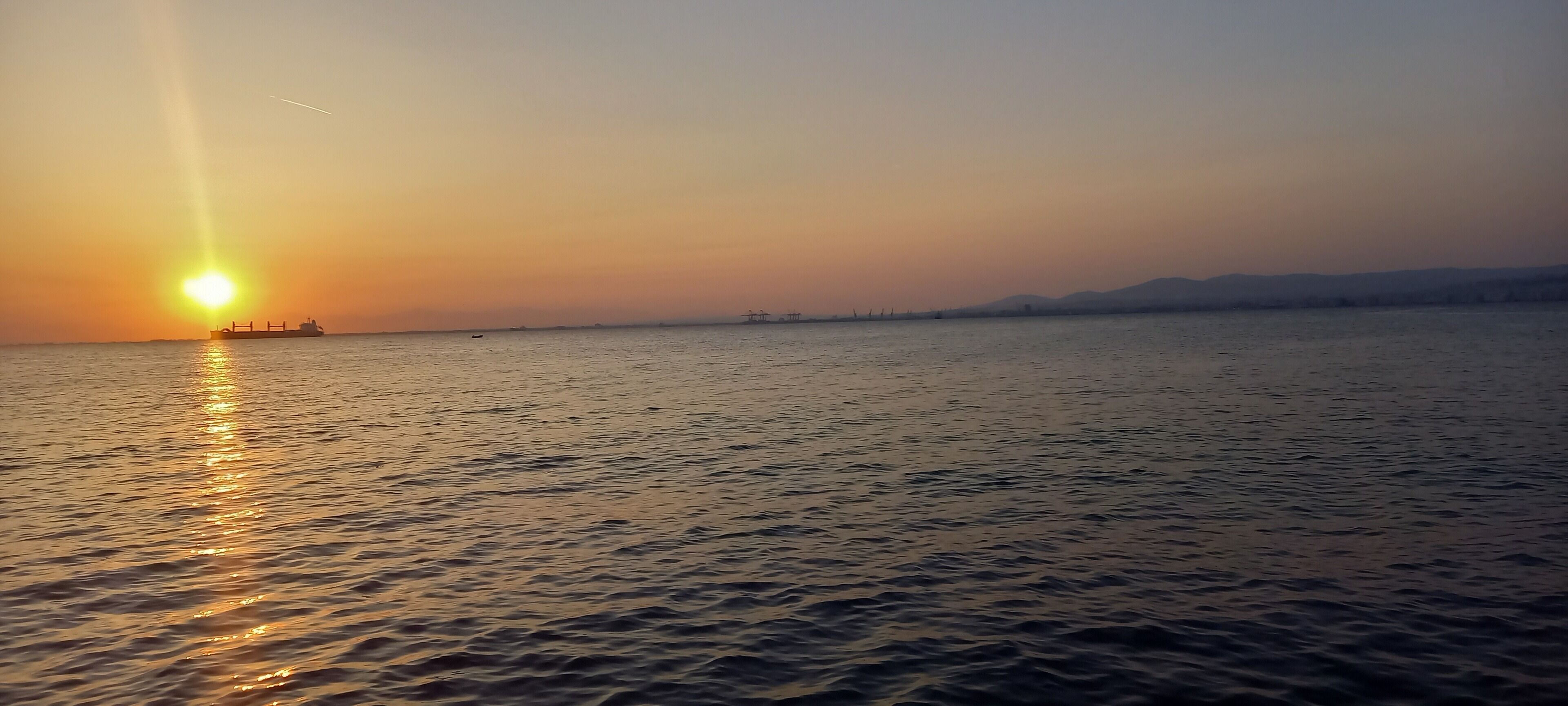 A calm body of water with a ship and distant land in the background.