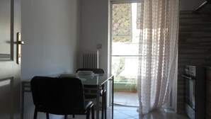 Uma área de refeições com mesa e cadeiras, uma janela com cortinas e uma cozinha com fogão.