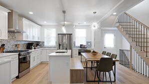 Una cocina moderna con armarios blancos, una isla central y un comedor con mesa y sillas de madera.