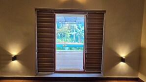 Een kamer met een groot raam met gesloten luiken, een wandlamp boven het raam en een betegelde vloer.