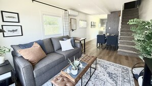 Una sala de estar moderna con un sofá gris, una mesa de centro y una escalera que lleva a un comedor.