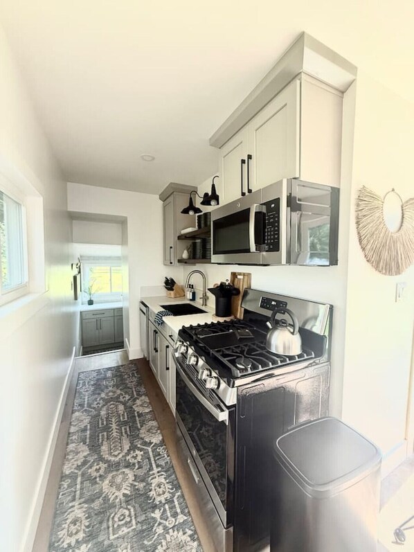 A modern kitchen with white cabinetry, a gas stove, a microwave, and a sink.