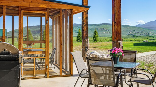 A wooden structure with a table and chairs, a grill, and a view of a green landscape with hills. - Studio Cabin w/ Mtn Views by the Green River! (Cora)