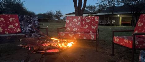 A fire pit with chairs around it, a tree, and a building in the background.