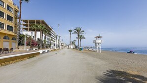A beachside promenade with a row of buildings, palm trees, and a lifeguard tower.