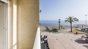 A balcony with a view of a beach, palm trees, and a clear sky.