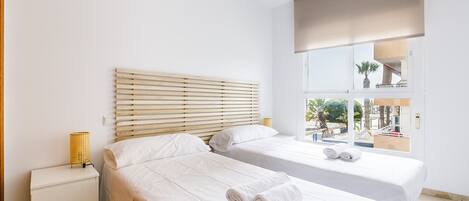 A modern hotel room with two beds, a bedside table, a lamp, and a large window with a view.