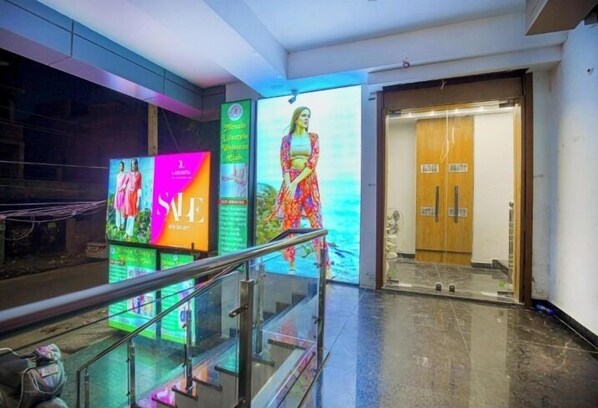 A hotel lobby with a glass railing, a large digital advertisement, and a wooden door.