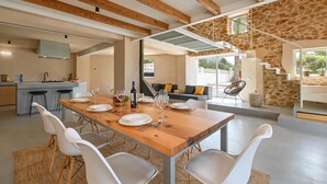 A modern dining area with a wooden table set for six, white chairs, and a kitchen in the background. - La de Ros - Javea, Costa Blanca (Javea)