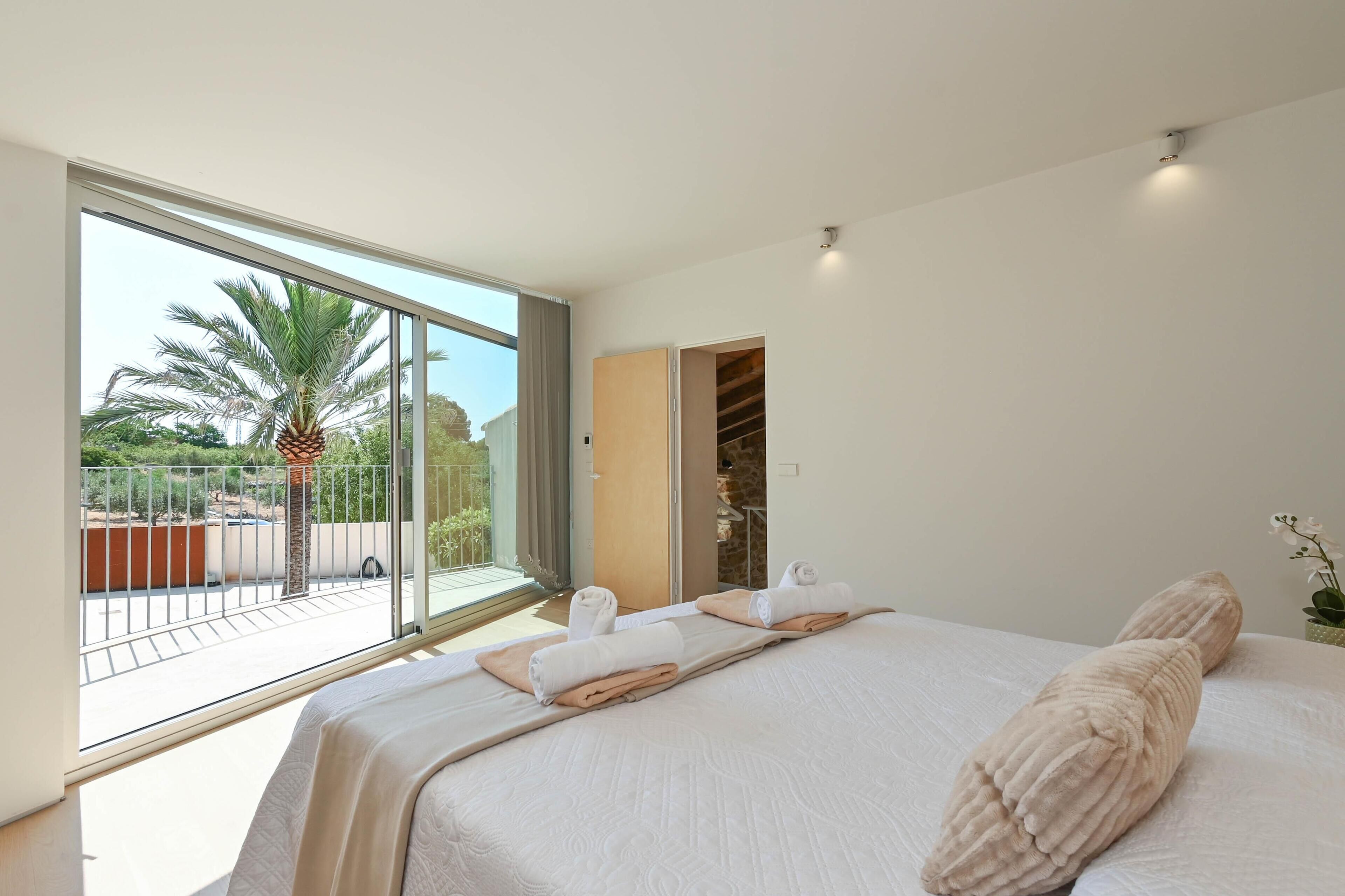 A modern hotel room with a large bed, a balcony with a palm tree, and a view of the outdoors.