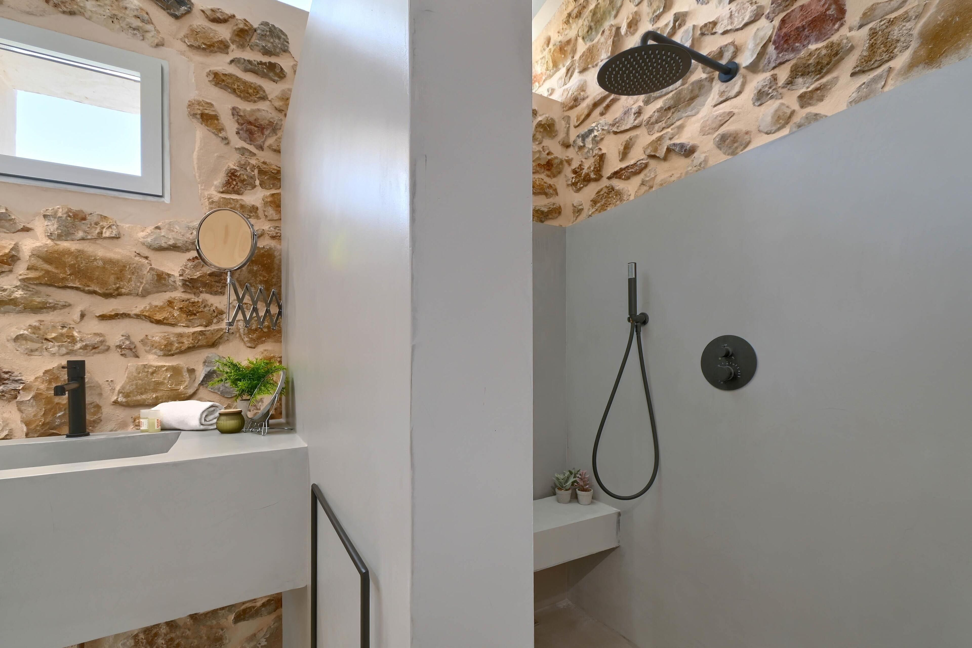 A bathroom with a stone wall, a mirror, a towel, and a shower.