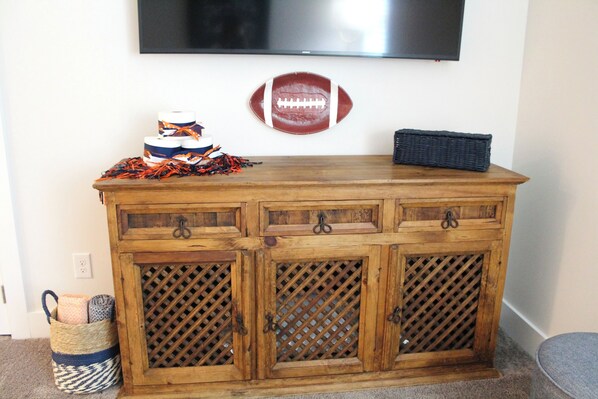 A wooden cabinet with drawers and a lattice front, a flat-screen TV mounted above it, and a football decoration on the wall.