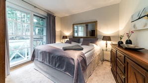 Ein Schlafzimmer mit einem großen Bett, einem Schminktisch, einem Spiegel und einem Fenster mit Vorhängen.