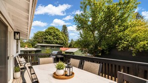 An outdoor patio with a marble table, chairs, a grill, and a potted plant.