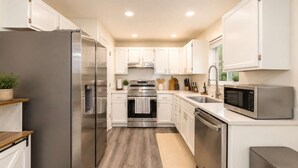A modern kitchen with stainless steel appliances, white cabinetry, and a wooden floor.